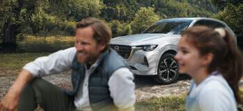 Der brandneue aufladbare Hybrid-SUV Mazda CX-60, abgebildet draußen in der Natur mit einem Mann und einer Frau, die in der Nähe sitzen.