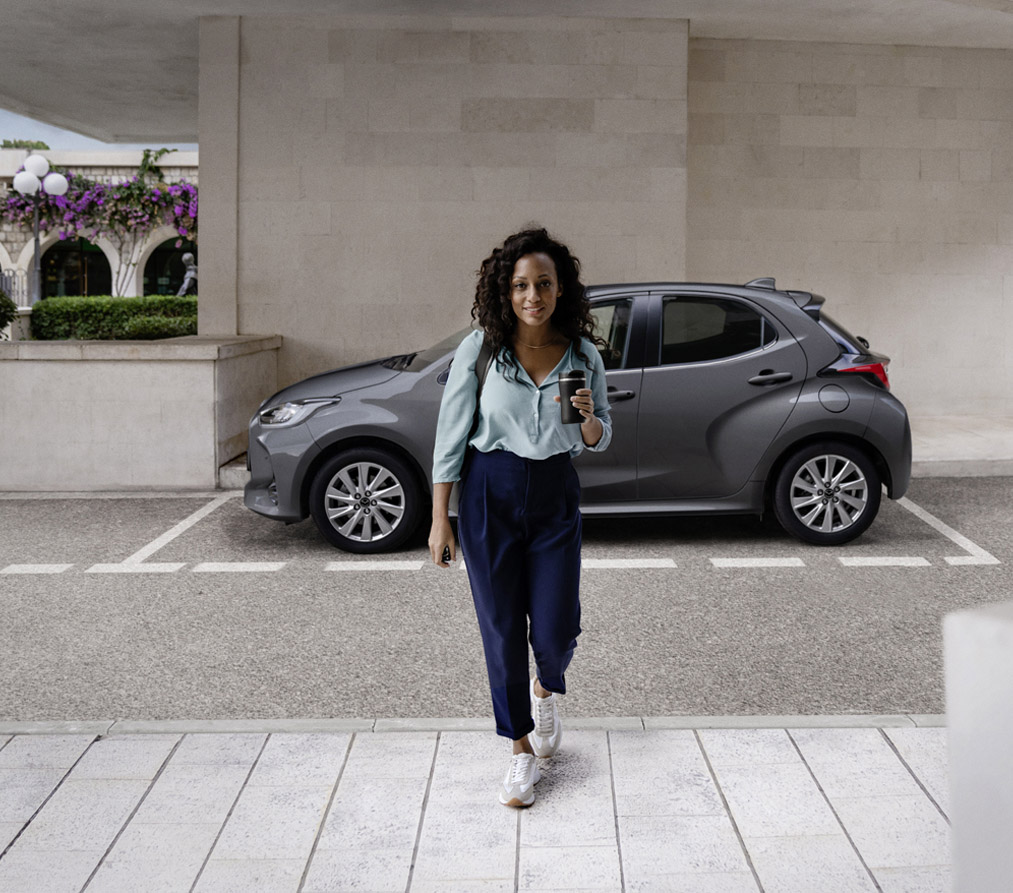 Nainen kävelee Mazda2 Hybridin edessä.
