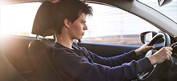 Ένας νεαρός άντρας μέσα σε ένα Mazda2 που οδηγεί σε έναν δρόμο.