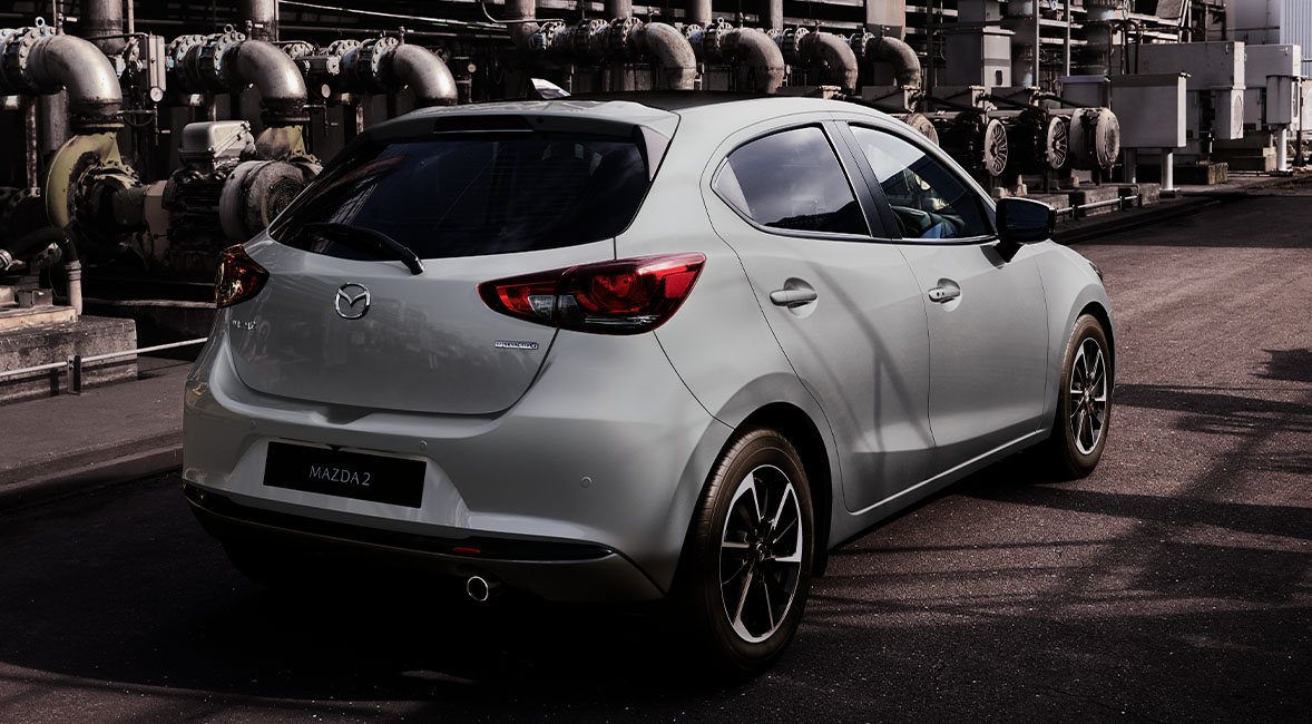 A grey Mazda2 pictured from the rear in an industrial landscape.