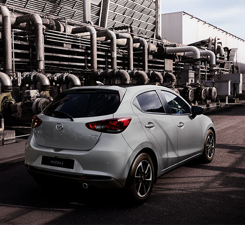 A grey Mazda2 pictured from the rear in an industrial landscape.