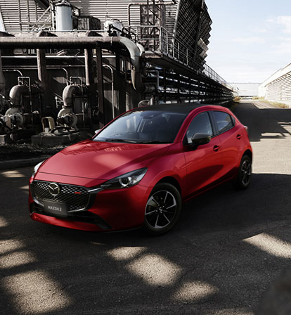 A red Mazda2 pictured from the front in an industrial landscape.