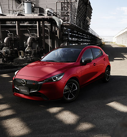 A red Mazda2 pictured from the front in an industrial landscape.