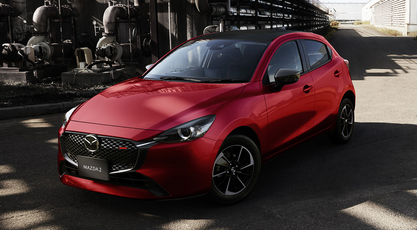 A red Mazda2 pictured from the front in an industrial landscape.