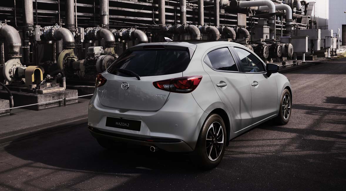 Una Mazda2 grigia ripresa da dietro in un paesaggio industriale.