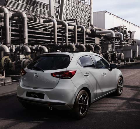 Una Mazda2 grigia ripresa da dietro in un paesaggio industriale.