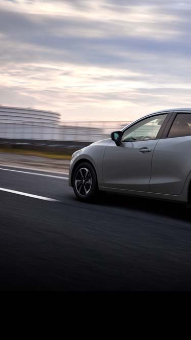 Una Mazda2 argentata che percorre una strada vista di lato.