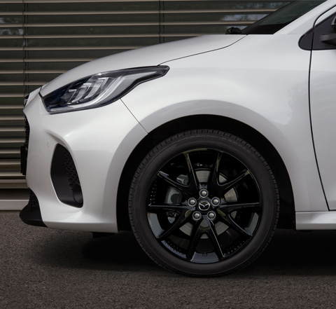 The front black alloy wheel of a white Mazda2 Hybrid.