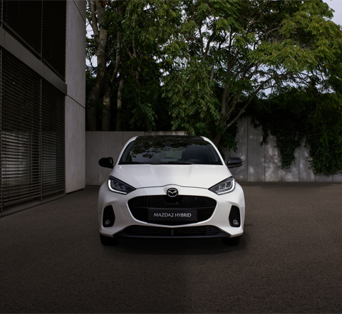 A white Mazda2 Hybrid parked showing its front end design and features.