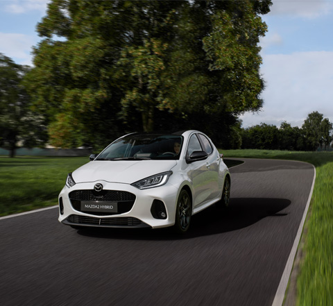 The Mazda2 Hybrid in white driving on the street.