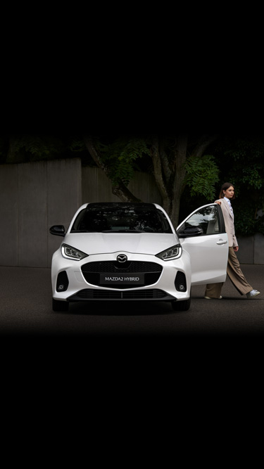 A woman standing next to the driver's side of the Mazda2 Hybrid.