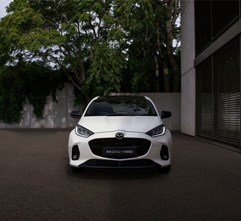 A white Mazda2 Hybrid parked showing its front end design and features.