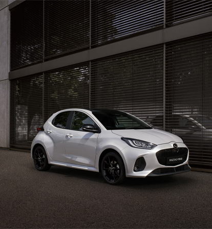 The Mazda2 Hybrid in white parked in front a building.