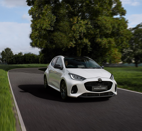 The Mazda2 Hybrid in white driving on the street.