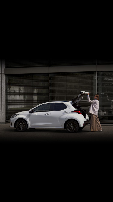 A woman opening the boot of the Mazda2 Hybrid in white.