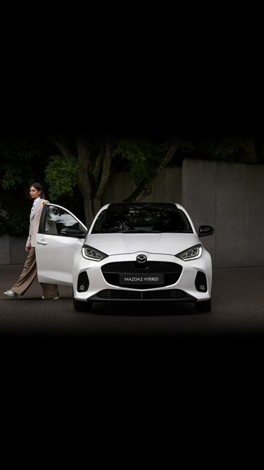 A woman standing next to the driver's side of the Mazda2 Hybrid.