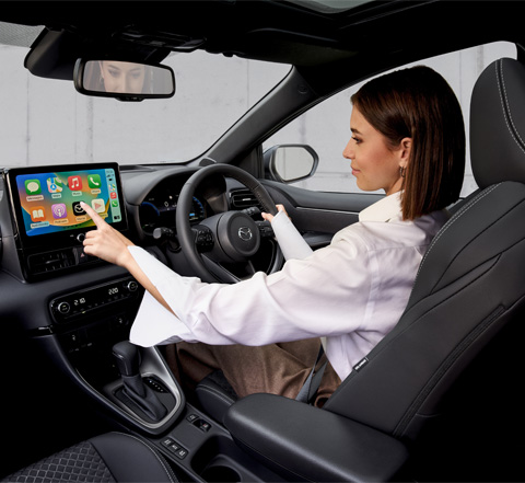 A woman using the touchscreen panel while driving the Mazda2 Hybrid.