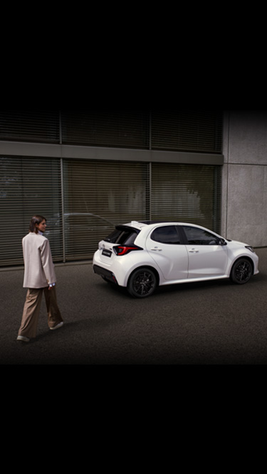 A white Mazda2 Hybrid seen the side parked in front of a building.