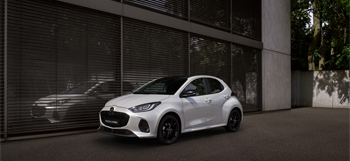 Valkoinen Mazda2 Hybrid pysäköitynä rakennuksen eteen.