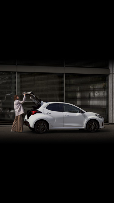 Une femme ouvrant le coffre d'une Mazda2 Hybrid blanche.