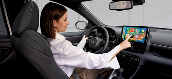 Une femme utilisant l'écran tactile en conduisant la Mazda2 Hybrid.