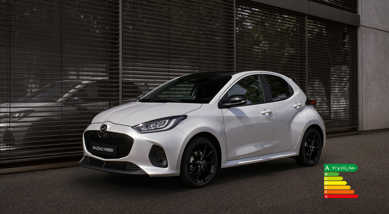 Mazda2 Hybrid de couleur blanche stationnée devant un bâtiment.