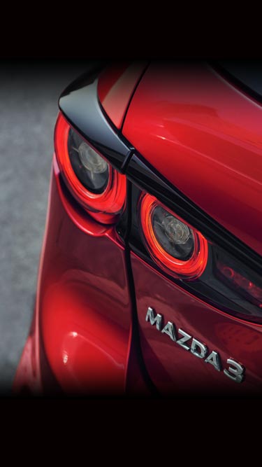 Задните комбинирани светлини на червена Mazda3 и логото на Mazda3.