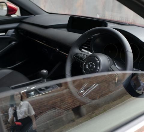 The beautiful steering wheel of the Madza 3 pictured through the half open window.