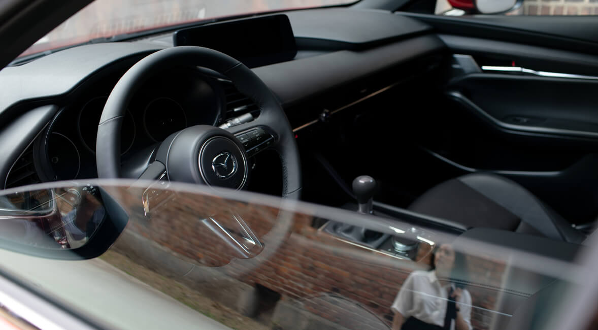 A Mazda3 gyönyörű megjelenésű kormánya látható a félig nyitott ablakon keresztül.