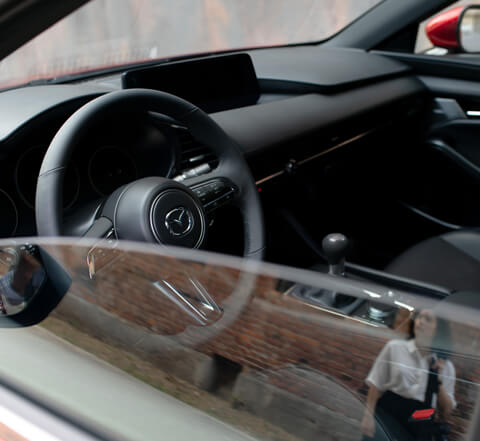 A Mazda3 gyönyörű megjelenésű kormánya látható a félig nyitott ablakon keresztül.