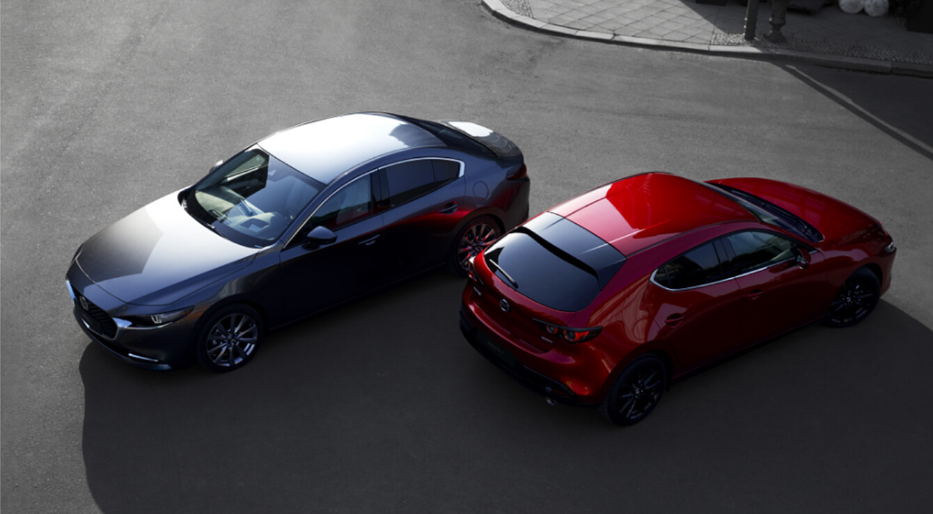 Fotografia da dianteira de um Mazda3 Sedan preto e da traseira de um Mazda3 Hatchback vermelho.