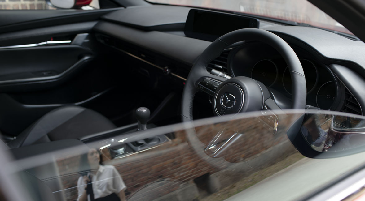 The beautiful steering wheel of the Madza 3 pictured through the half open window.