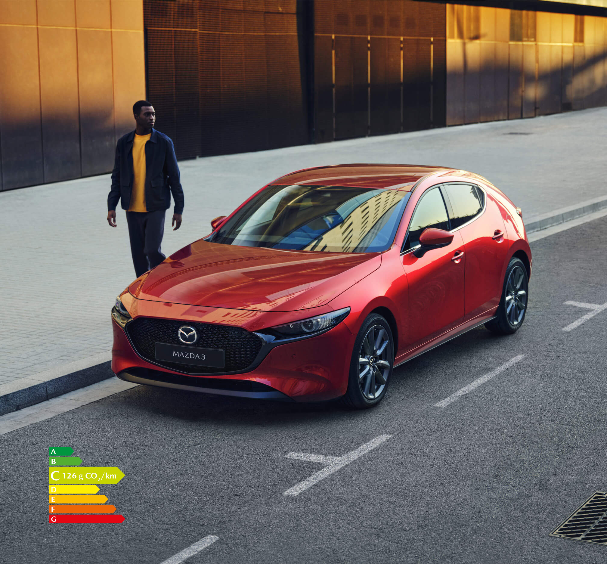 Homme avec un t-shirt jaune marchant à côté d’une Mazda3 5 portes rouge.