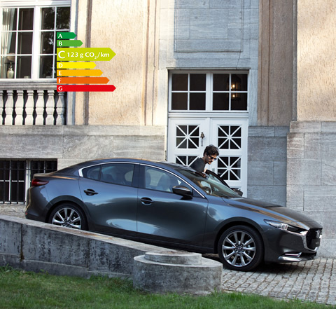 Mazda3 berline grise stationnée dans une allée en pente avec un homme marchant à côté.