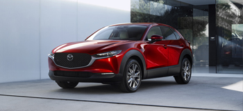 Partea din față a modelului Mazda CX-30 parcat în fața unei uși de sticlă.