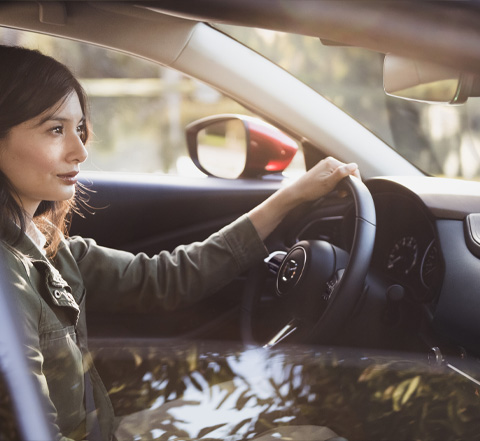 Eine Frau sitzt hinter dem Lenkrad eines Mazda CX-30 und fährt eine Straße entlang.