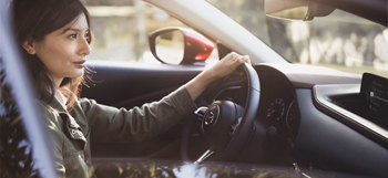 Woman behind the wheel of the Mazda CX-30, driving down the road.