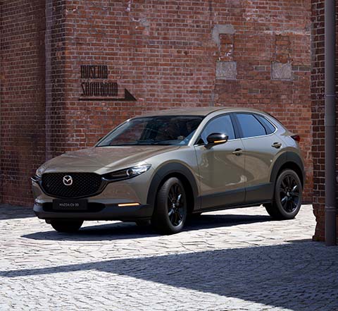 Mazda CX-30 Nagisa Special Version set forfra parkeret ved siden af en murstensbygning.