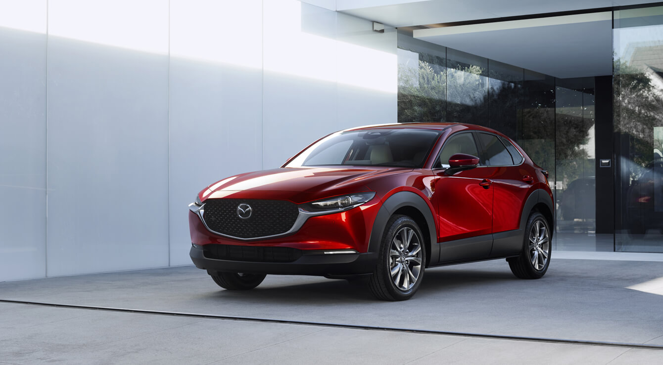 Vorderansicht eines Mazda CX-30, der vor einer Glastür geparkt ist.