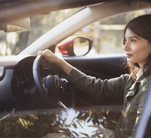 Woman behind the wheel of the Mazda CX-30, driving down the road.