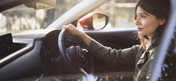 Woman behind the wheel of the Mazda CX-30, driving down the road.