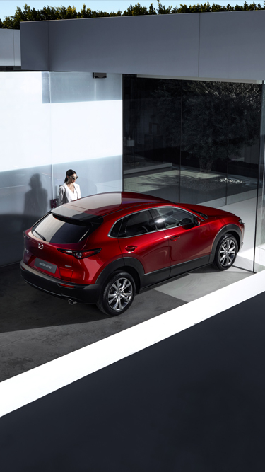 Vue du haut du nouveau Mazda CX-30 en rouge, garé à côté d’une femme.