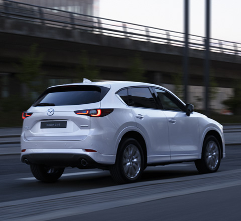 A white 2023 Mazda CX-5 driving down a road picture from the rear.