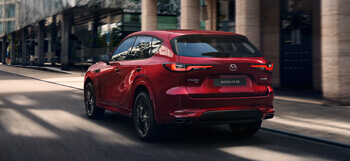 Zcela nové plug-in hybridní SUV Mazda CX-60 zaparkované před městskou budovou, zobrazené zezadu.