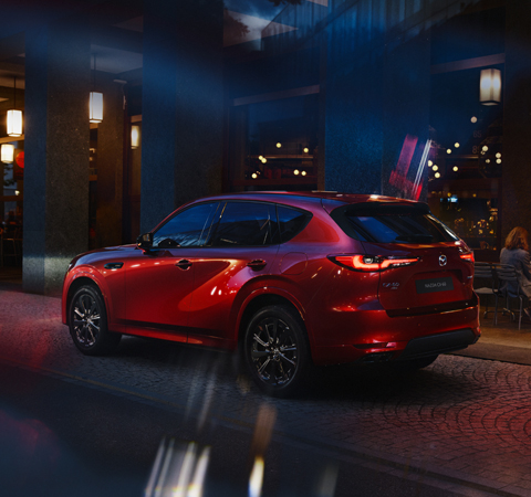Der brandneue aufladbare Hybrid-SUV Mazda CX-60 von hinten, geparkt bei Nacht in einer Stadt.