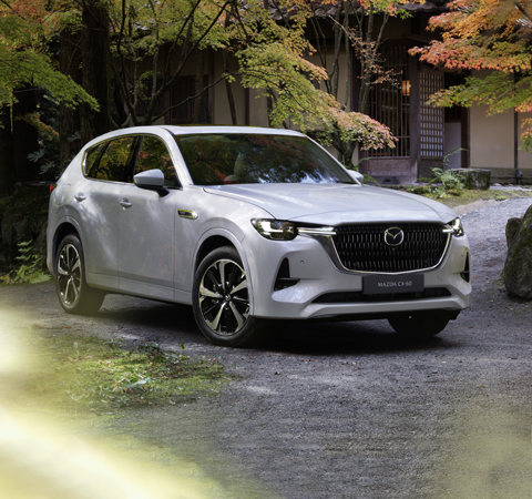 Der neue Mazda CX-60 Plug-In Hybrid SUV in der Frontansicht geparkt im Freien neben Bäumen.