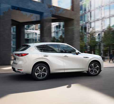 La All-New Mazda CX-60 SUV hybride rechargeable vue de côté roulant dans une rue en milieu urbain.