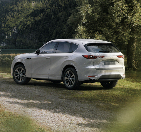 La All-New Mazda CX-60 SUV hybride rechargeable vue de l’arrière garée à l’extérieur dans un champ rempli d’arbres.