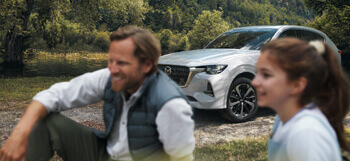 Immagine del nuovo SUV Mazda Ibrido Plug-In CX-60 fuori nella natura con un uomo e una donna seduti vicino.