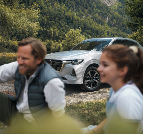 Un bărbat râzând și o femeie stând în fața noului SUV hibrid plug-in Mazda CX-60.